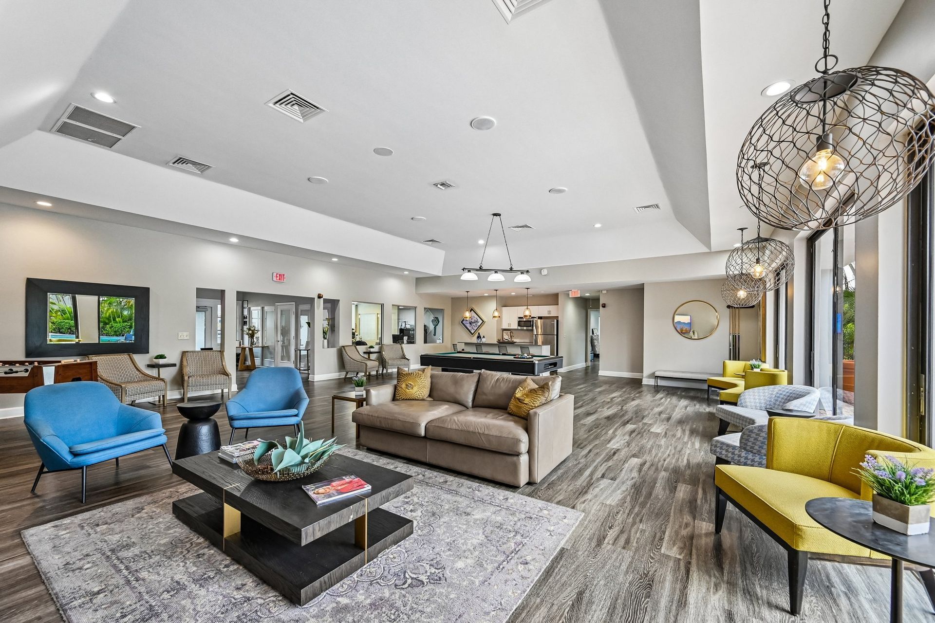 Bright modern living room with blue chairs, beige sofa, yellow bench, and large windows.