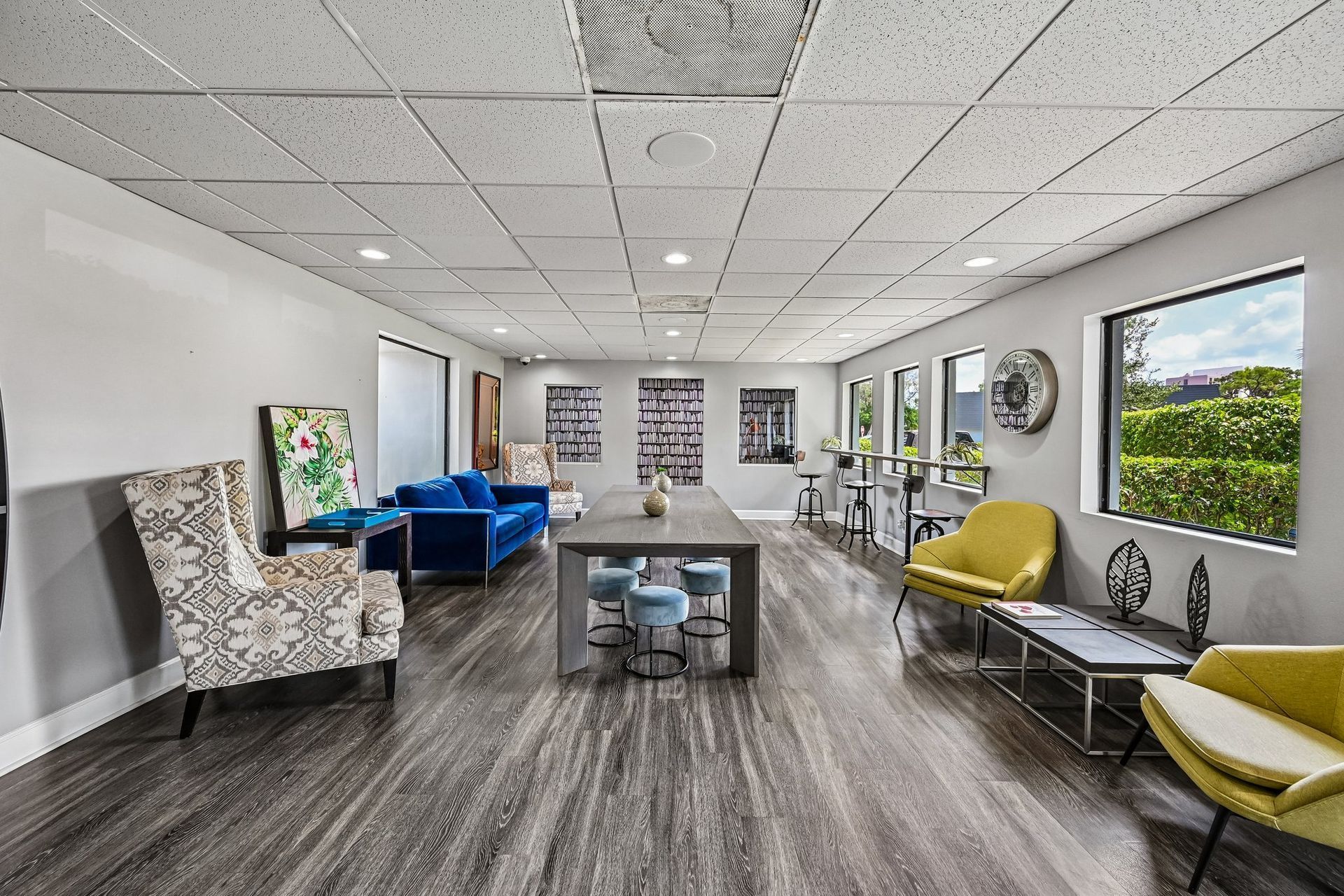 Bright office lounge with blue and yellow chairs, tables, and large windows with green views.