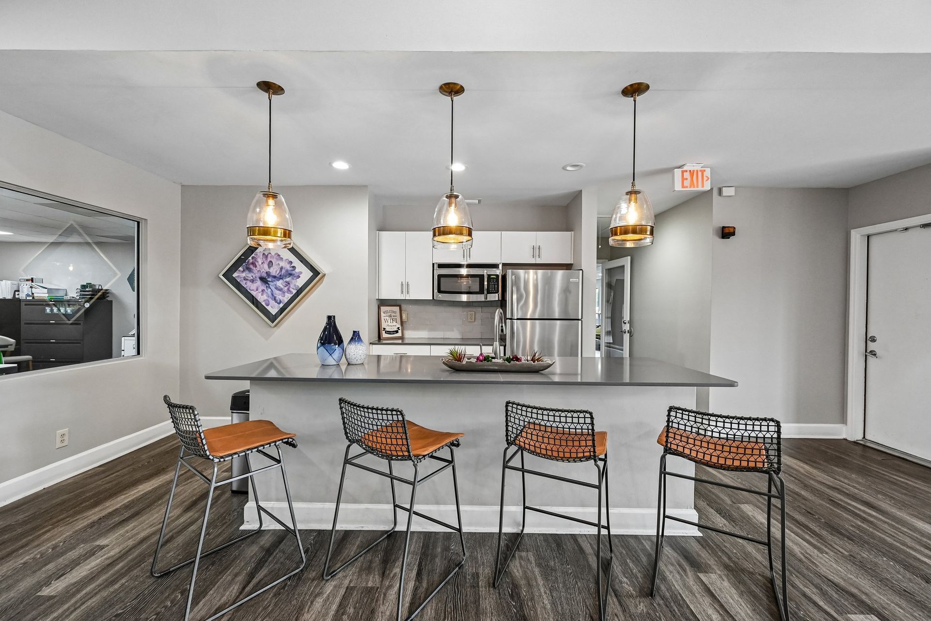 Modern kitchen and dining area with gray bar stools, pendant lights, and stainless steel appliances.