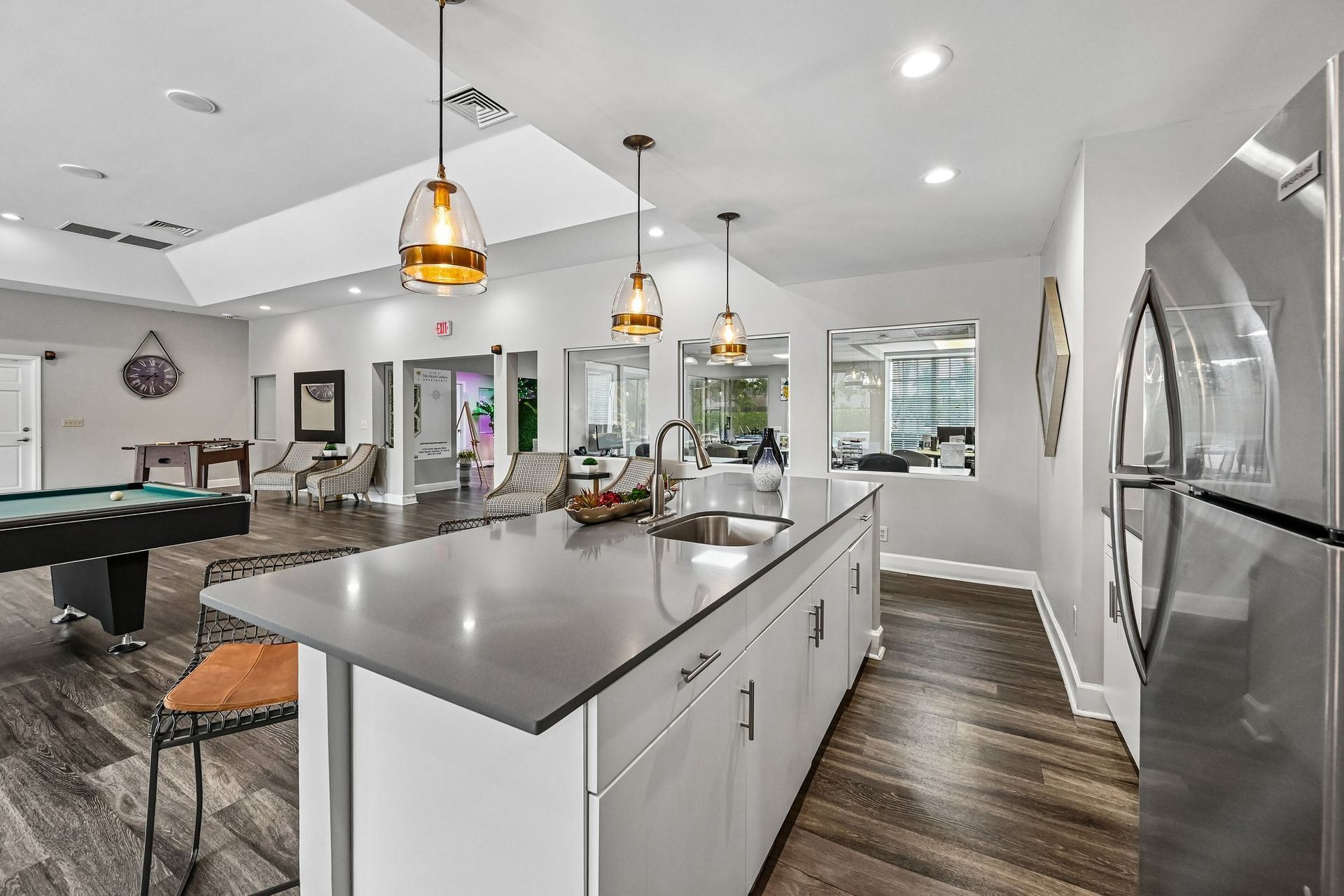 Bright modern kitchen with white cabinets, gray island, pendant lights, and stainless steel fridge.