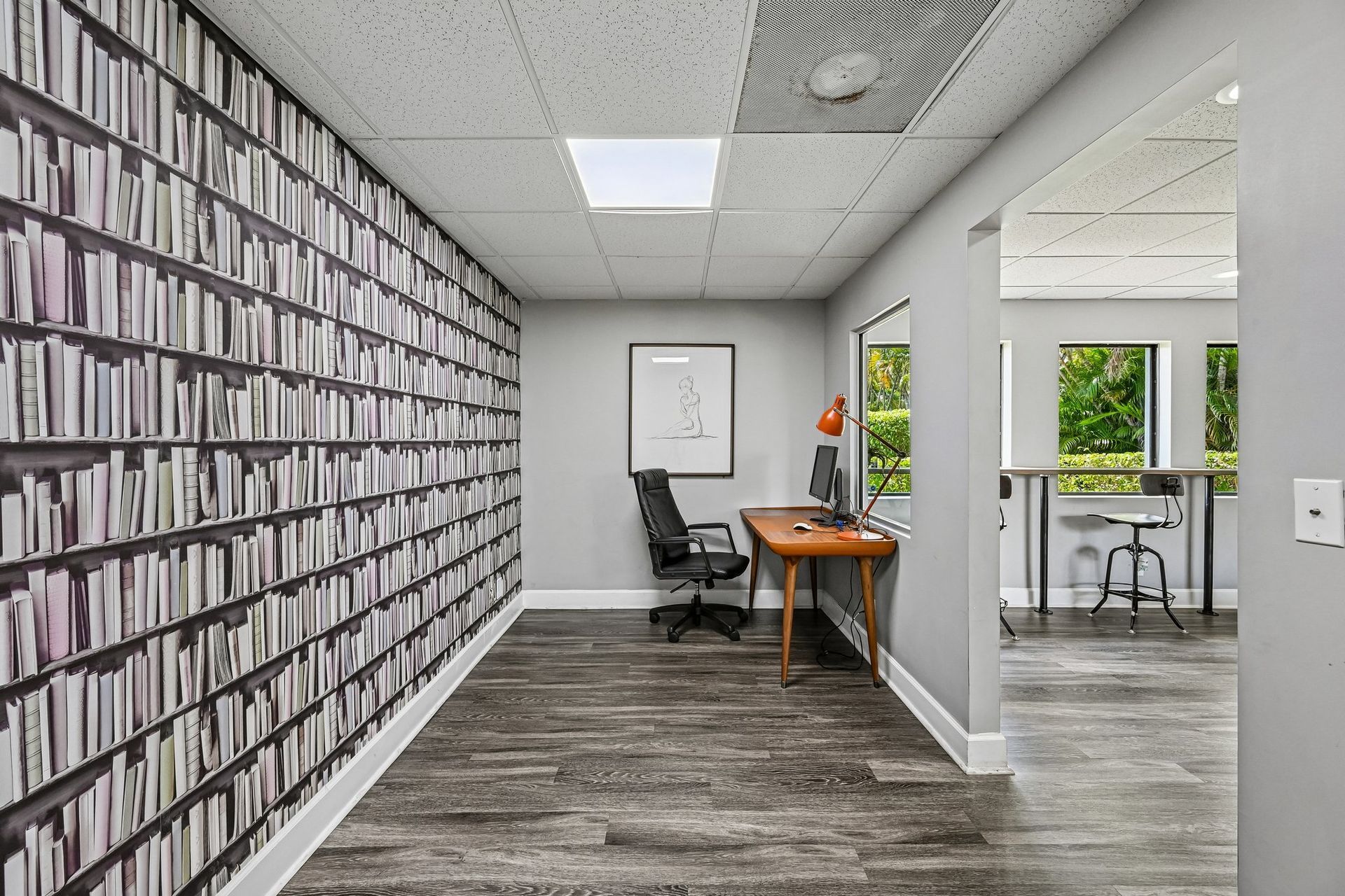 Modern office hallway with patterned wall, small desk, chair, and glass-walled workspace beyond.