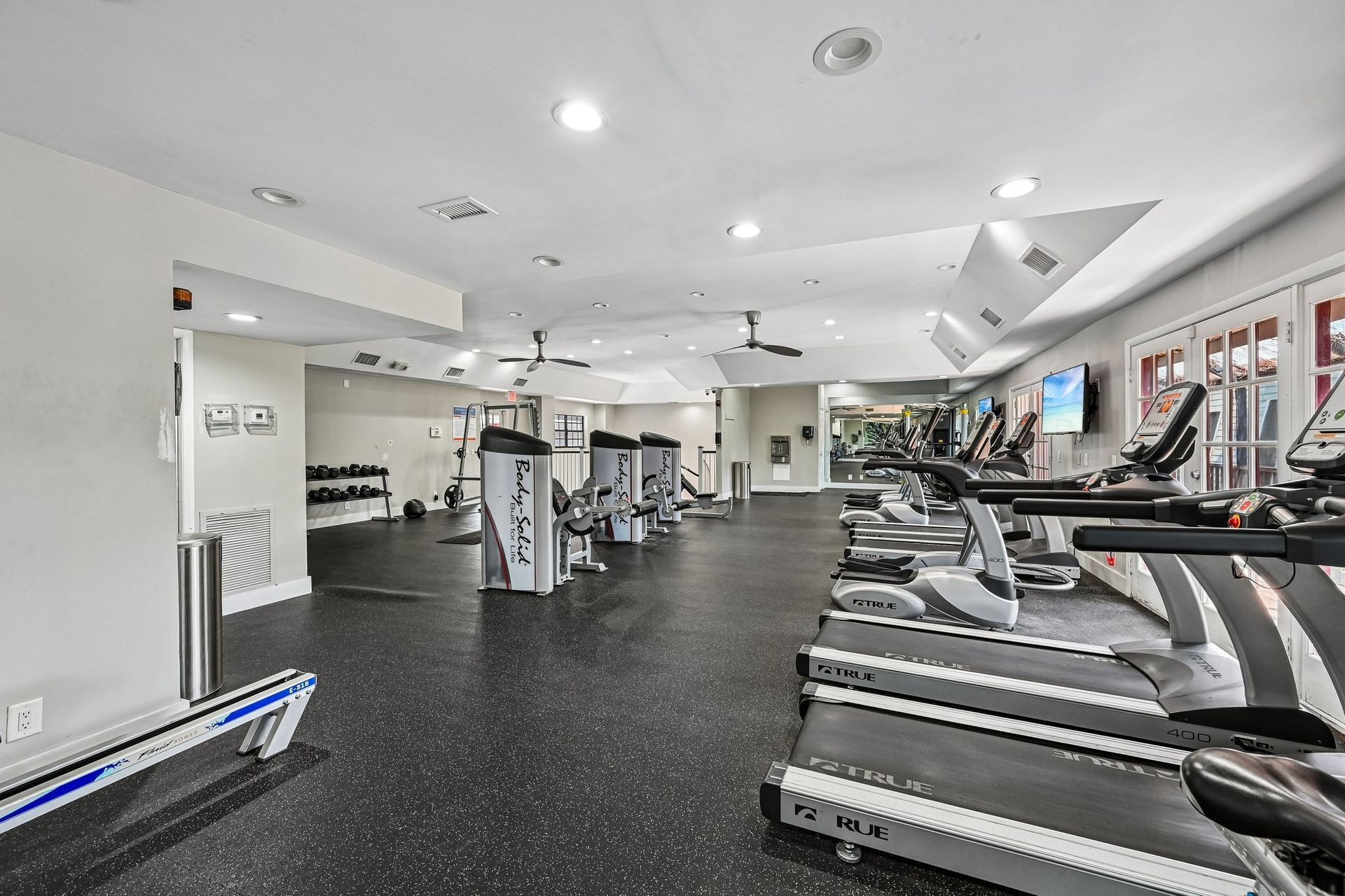 Bright gym interior with treadmills, weight machines, and mirrors on black flooring.