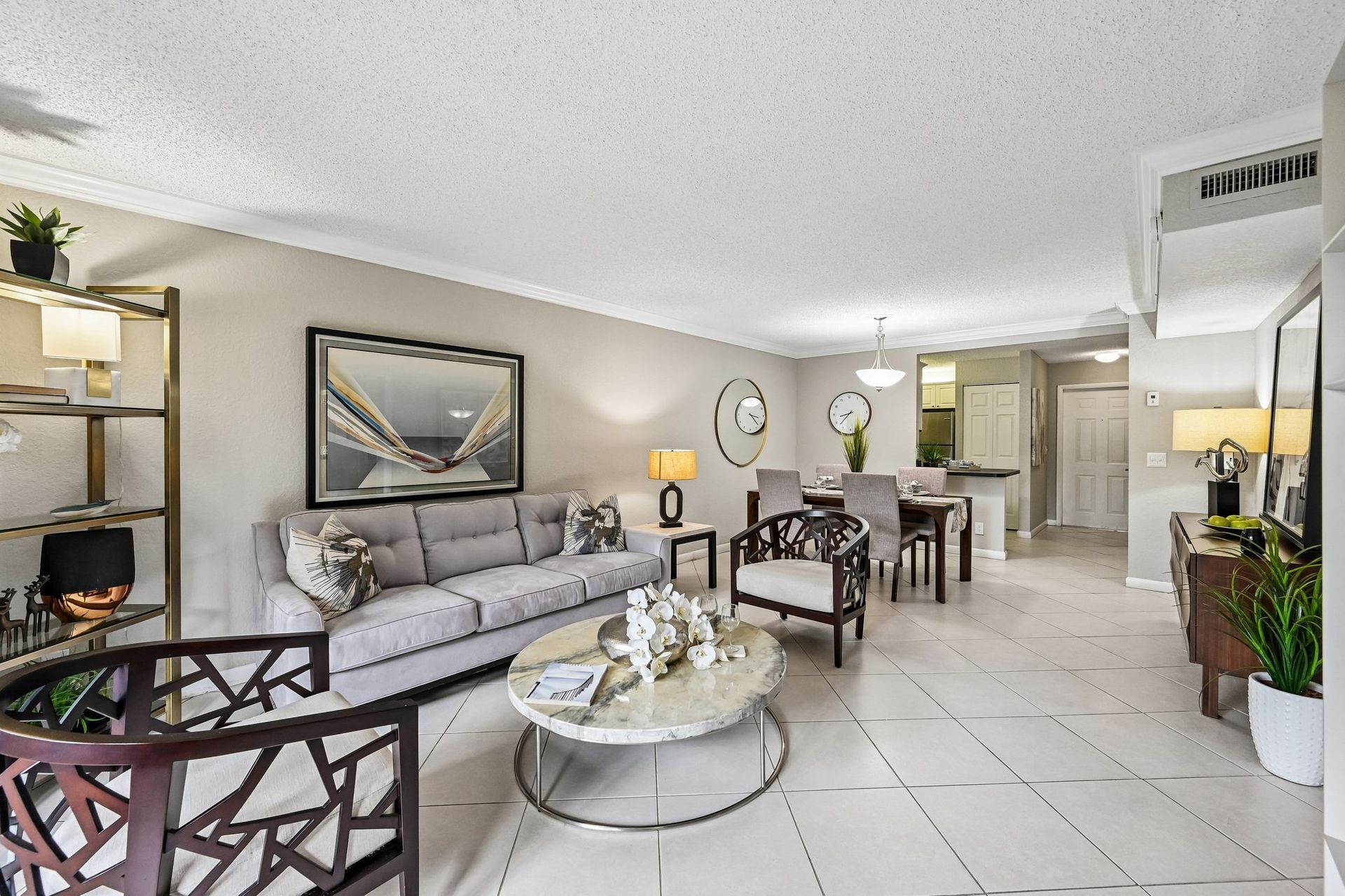 Bright modern living room with gray sofa, glass coffee table, dining area, and white tiled floor.