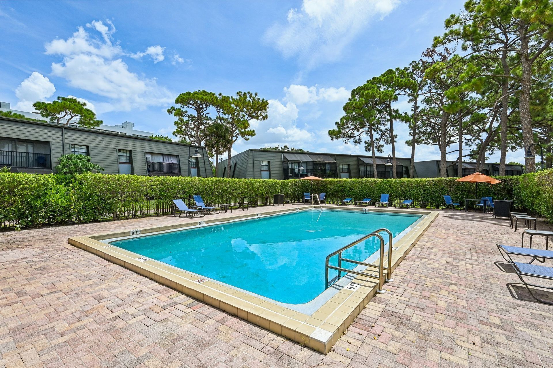 Outdoor swimming pool with turquoise water, lounge chairs, and trees beside a residential building.