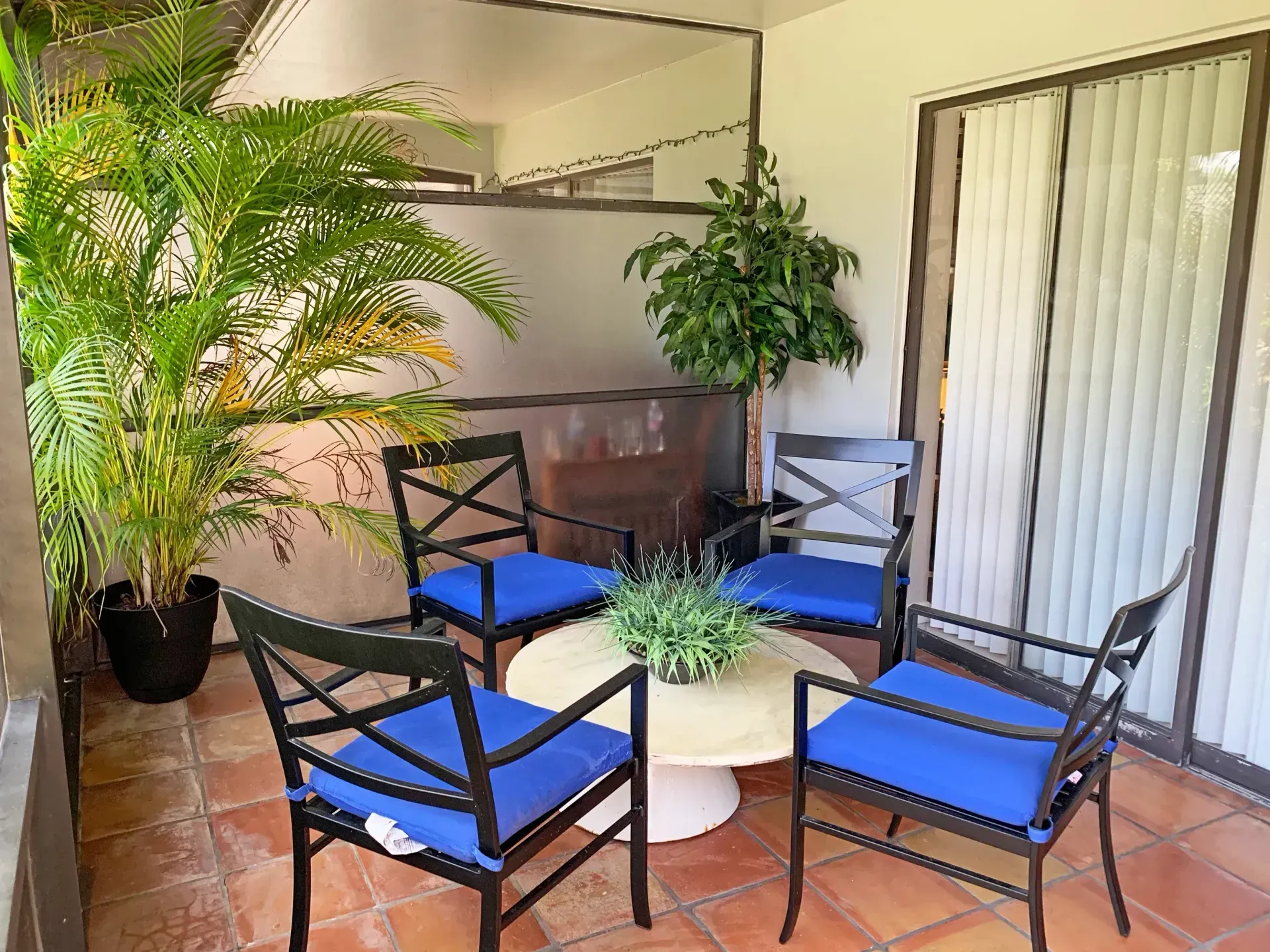 Patio seating area with black chairs, blue cushions, round table, and potted plants under a covered porch.