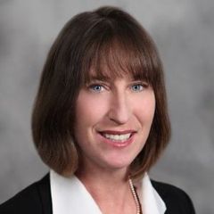 A woman in a suit and white shirt is smiling for the camera.