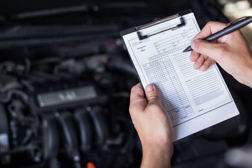 A Person Is Writing On A Clipboard In Front Of A Car Engine — Warren Ridge Auto Centre In Berkeley Vale, NSW