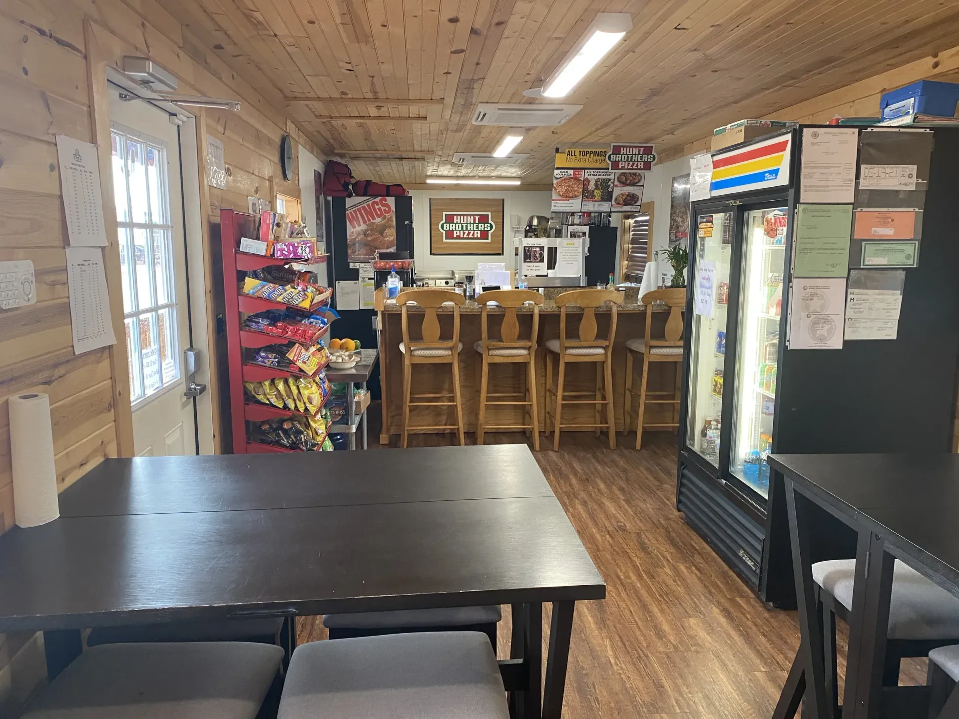 Cozy café interior with wooden bar stools, tables, and a refrigerated drink display case.