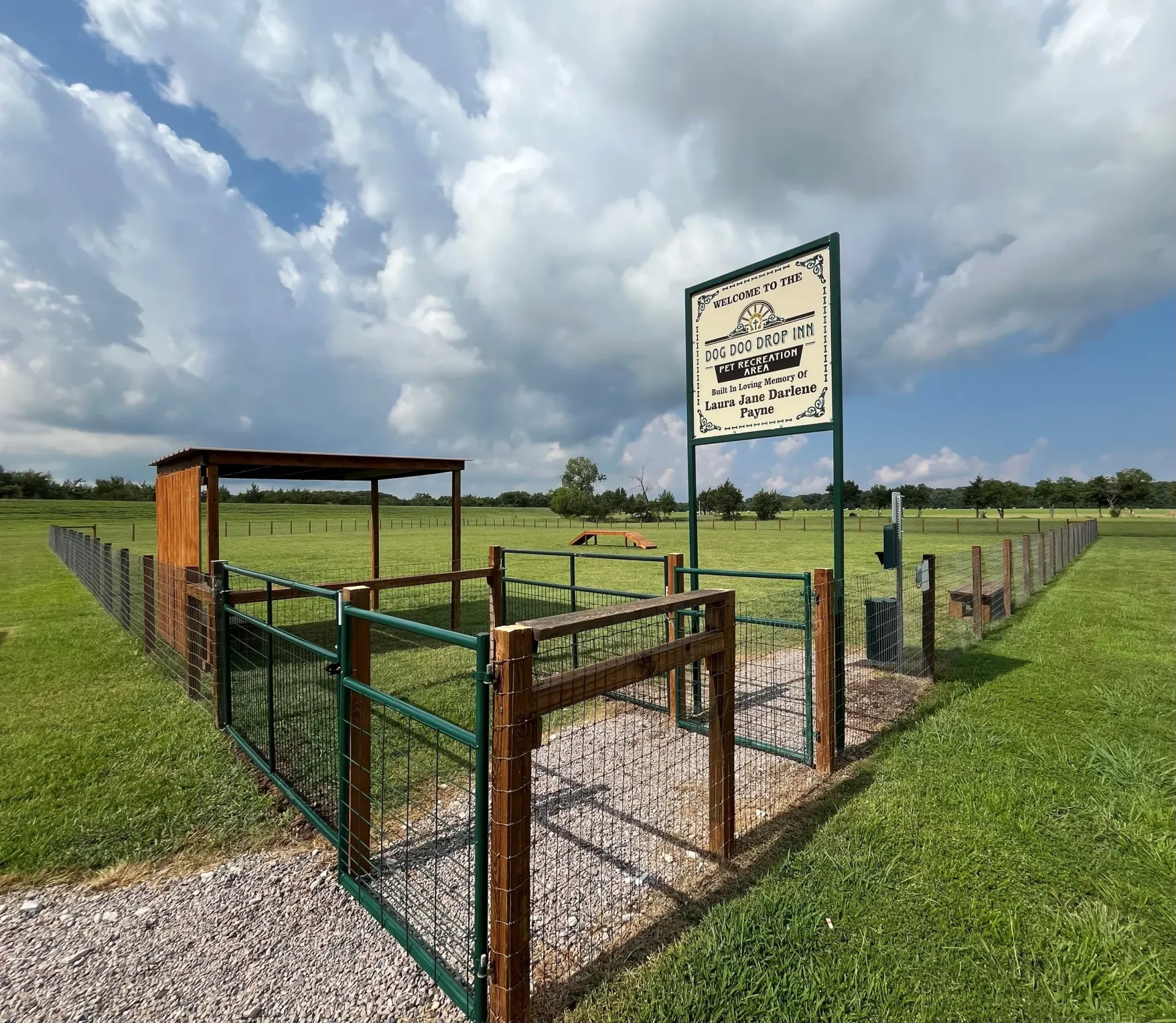Rusty fenced gate and sign at a grassy rural field under a cloudy sky