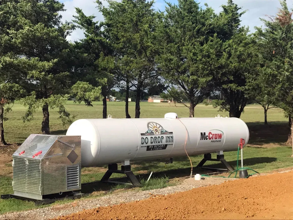 White propane tank and metal cage beside a dirt road with trees in the background