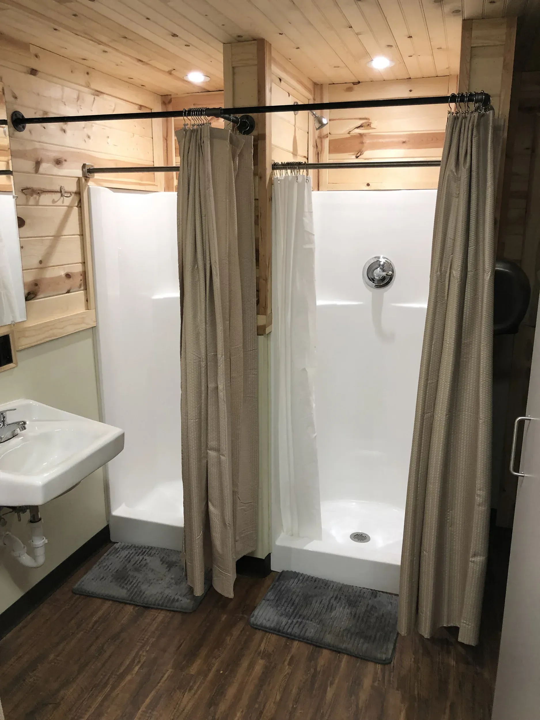 Wood-paneled bathroom with two curtained shower stalls and a wall-mounted sink
