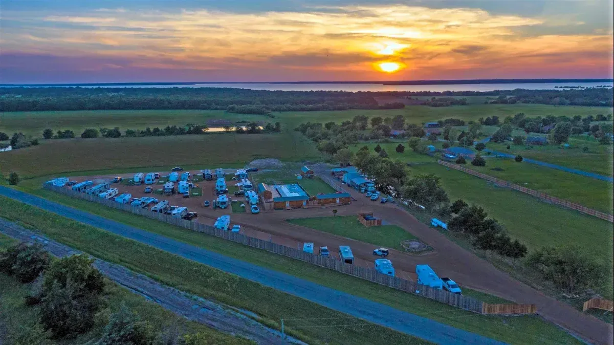 Aerial view of a rural campground at sunset with blue tents and parked vehicles amid green fields