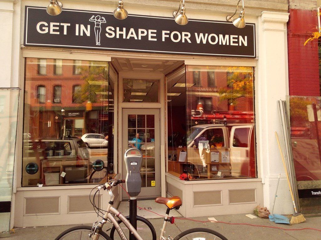 A bicycle is parked in front of a store called get in shape for women