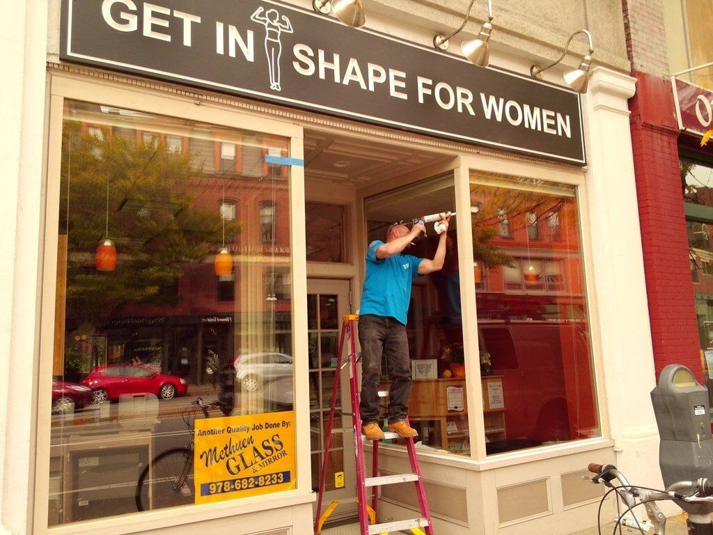 A man standing on a ladder in front of a store that says get in shape for women