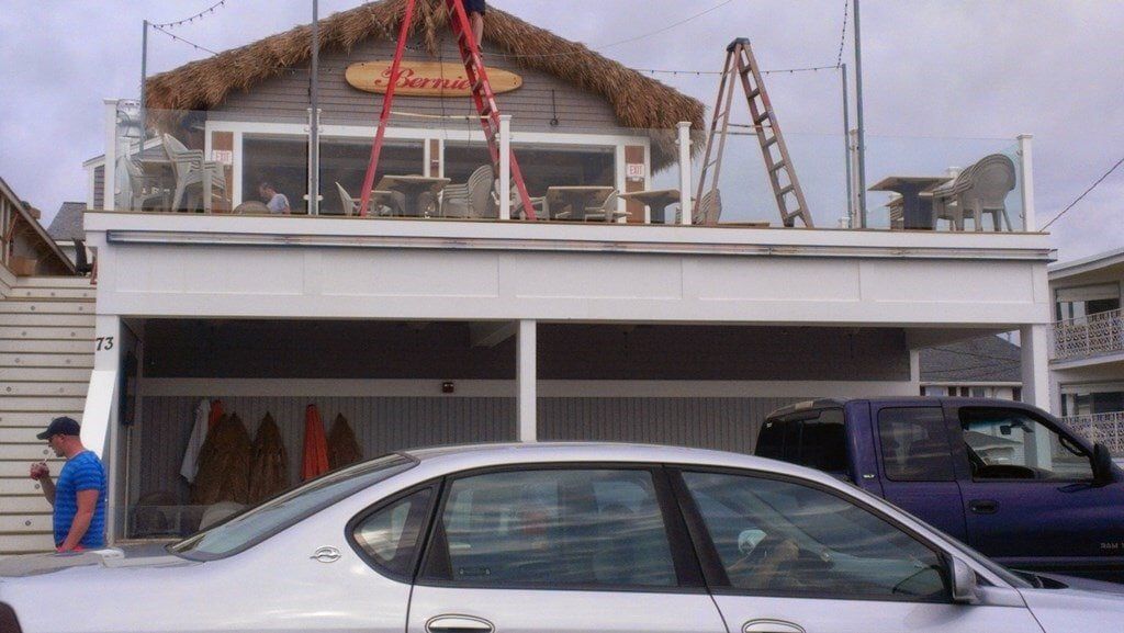A white car is parked in front of a building with a thatched roof