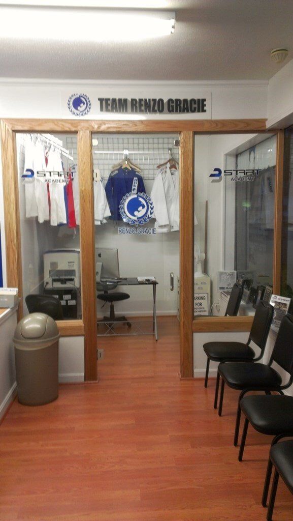 A waiting room with chairs , a trash can , a desk and a window.