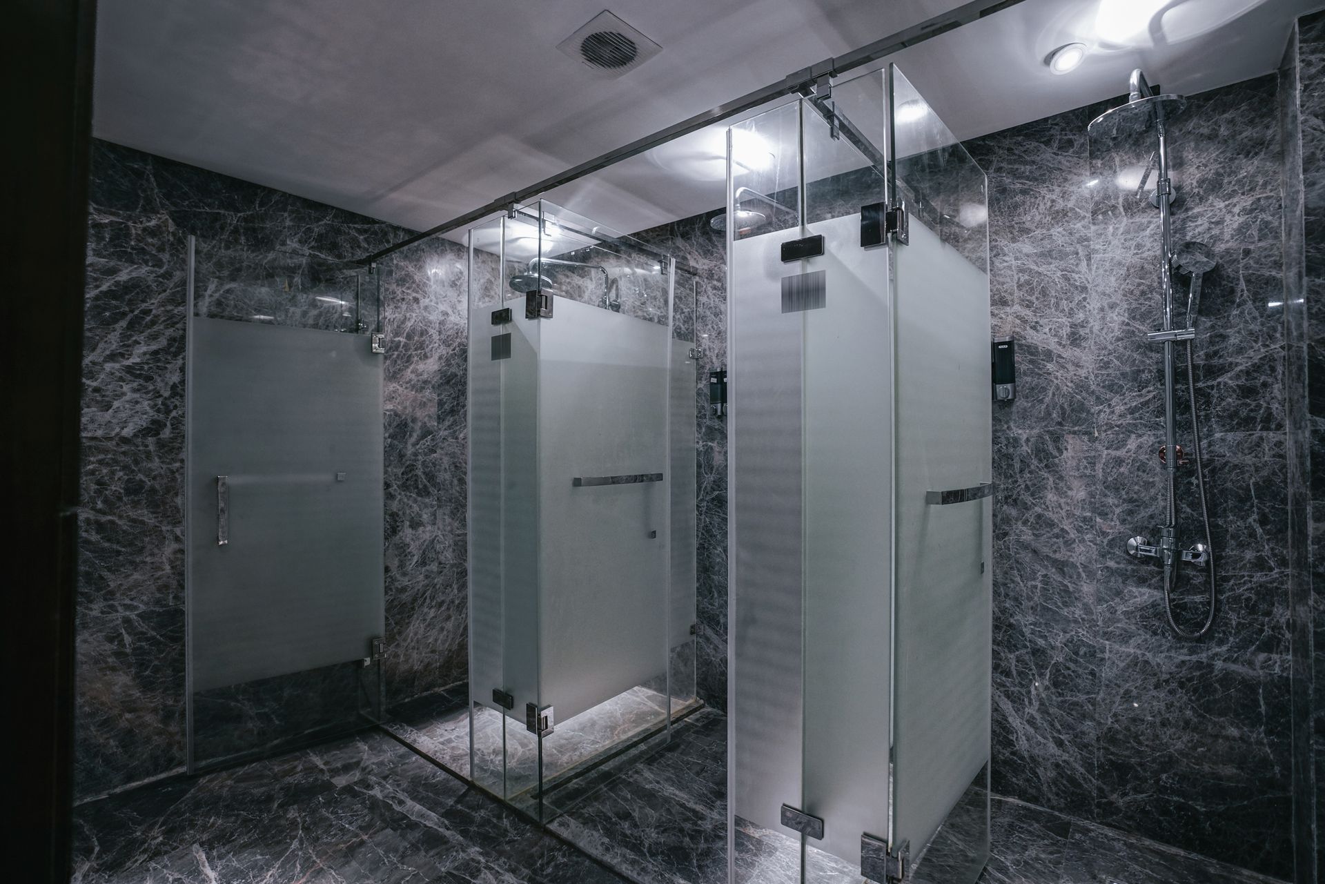 A bathroom with a lot of shower stalls and mirrors.