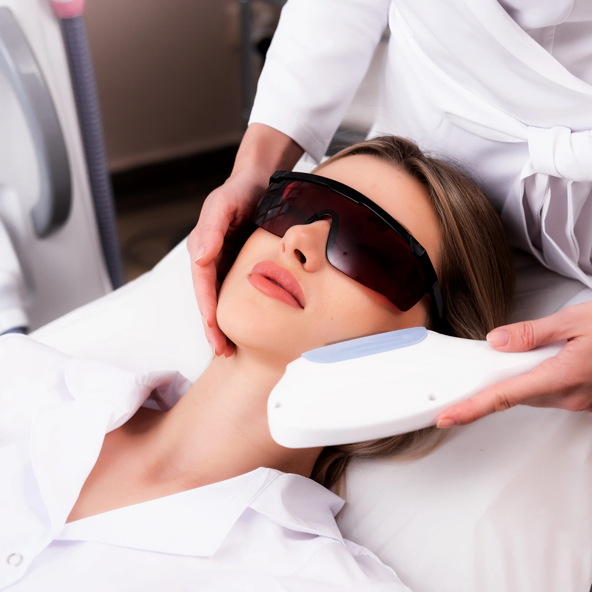 Woman receiving a facial treatment with a handheld device while wearing protective goggles