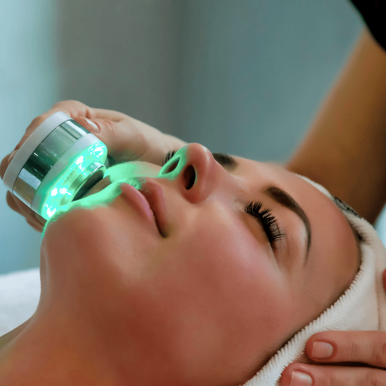 Woman receiving green LED facial treatment while lying on a spa bed