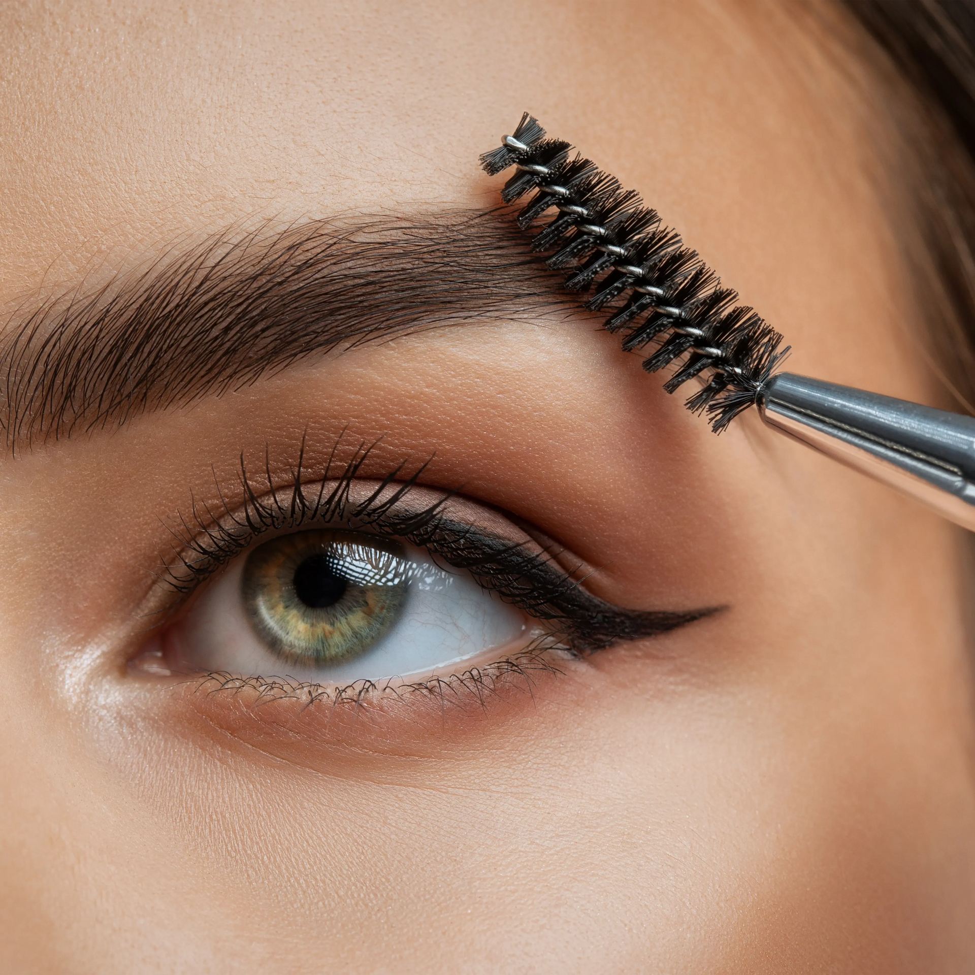 Close-up of an eye as a spoolie brush combs dark eyebrow hairs into shape.