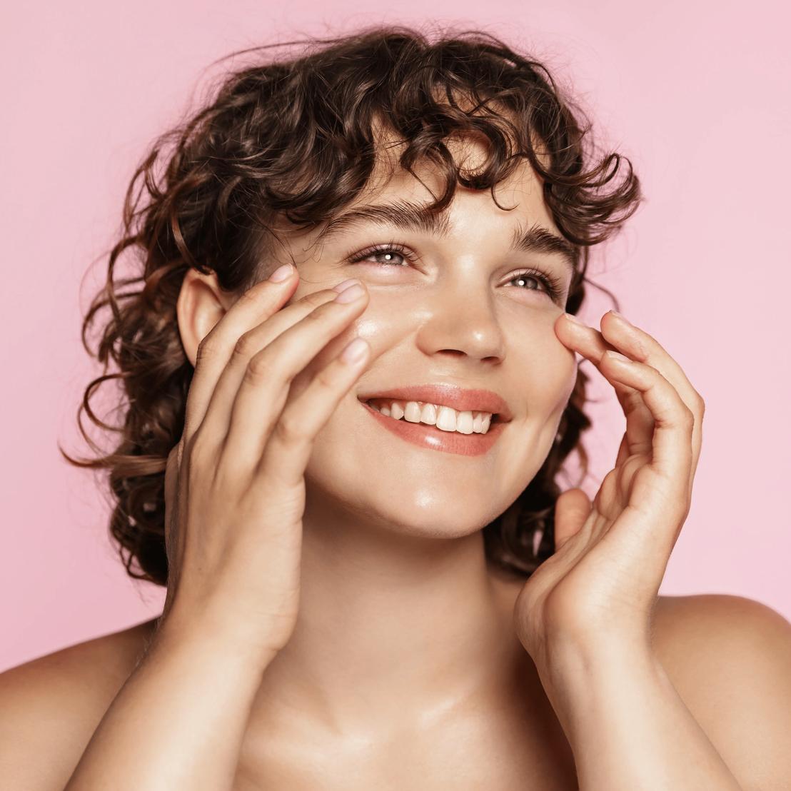 Smiling person touching their face against a pink background