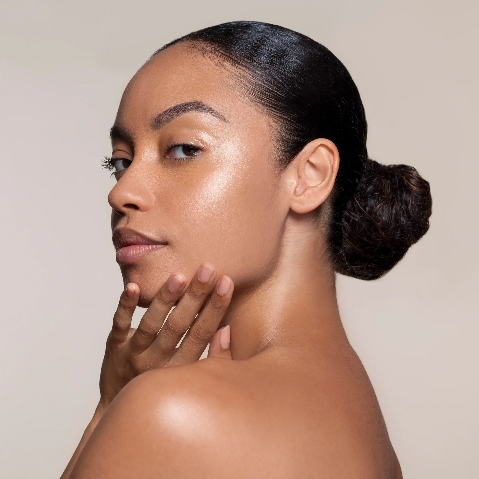 Portrait of a person with a sleek bun, resting a hand on the chin against a neutral background