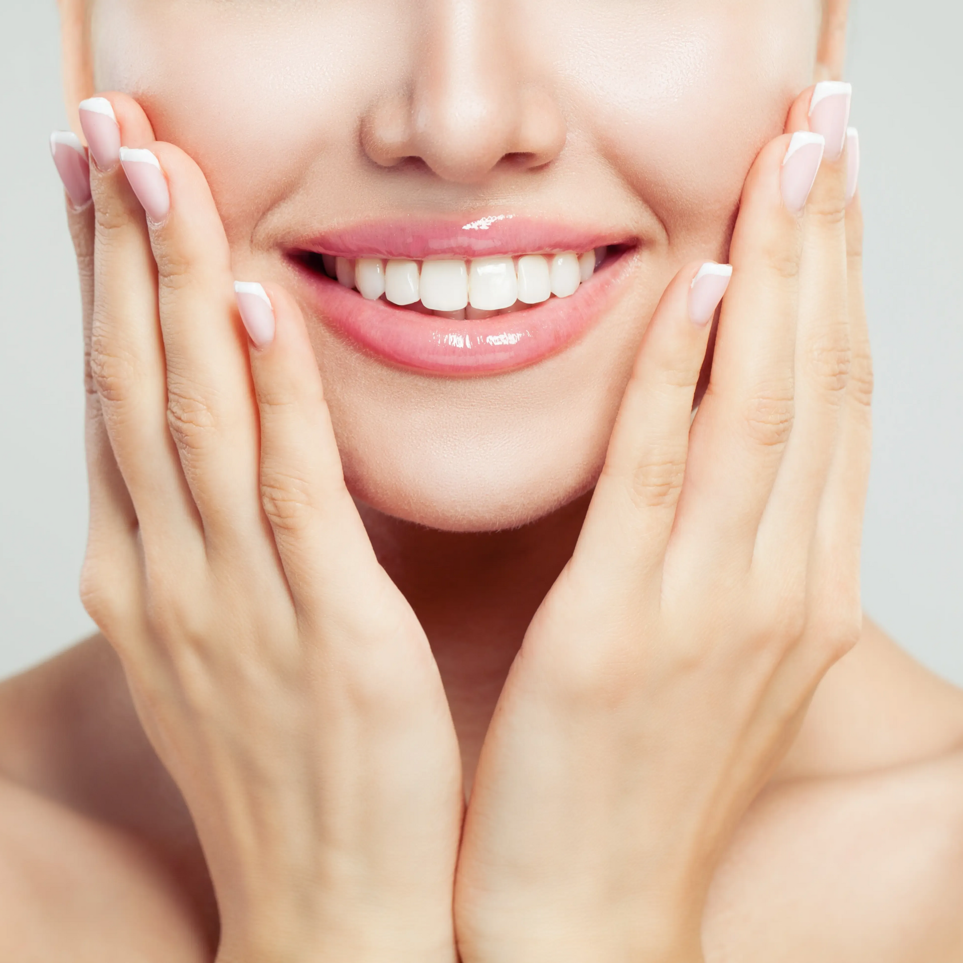 Smiling mouth with white teeth, framed by hands touching cheeks on a soft beige background