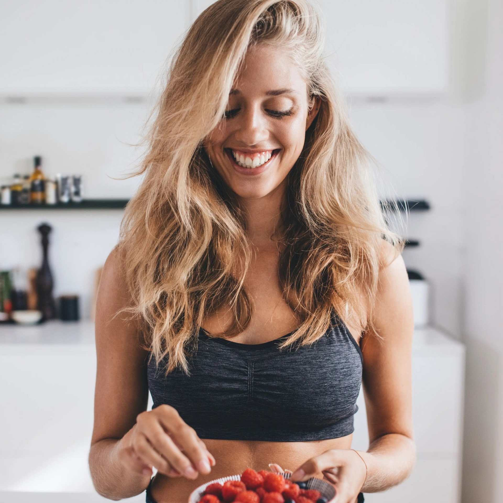 Smiling woman in a kitchen preparing food, holding a knife and cutting ingredients.