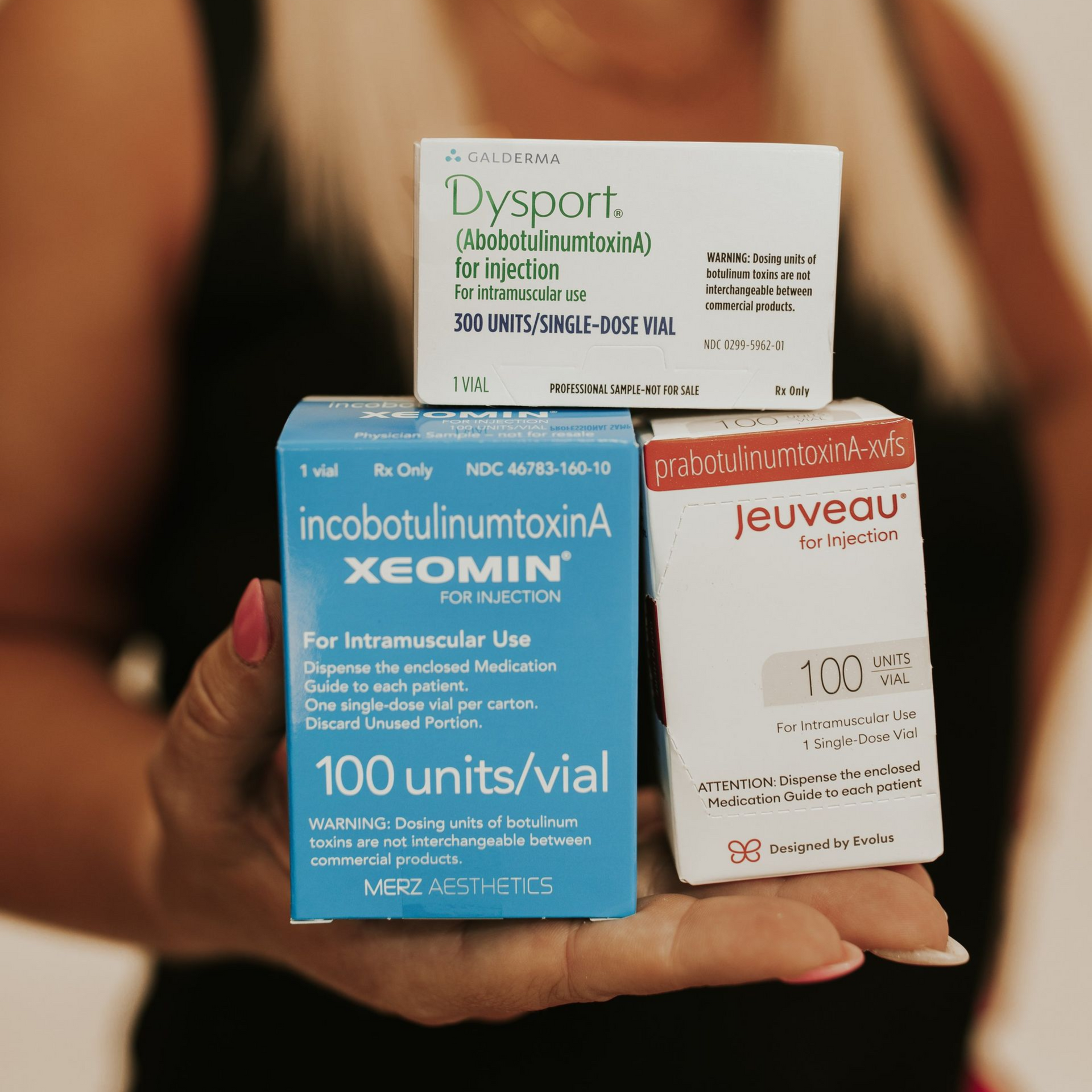 Hand holding three cosmetic injection boxes: Dysport, Xeomin, and Jeuveau.