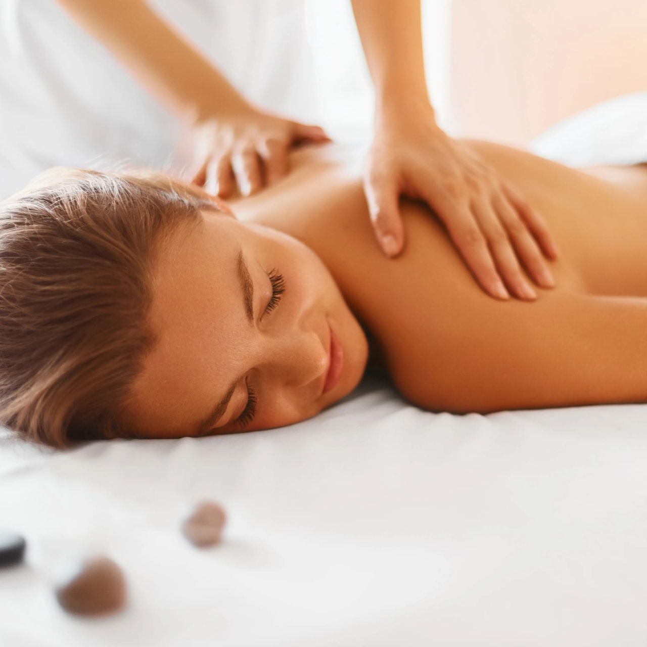 Person receiving a relaxing back massage on a white bed with soft spa lighting