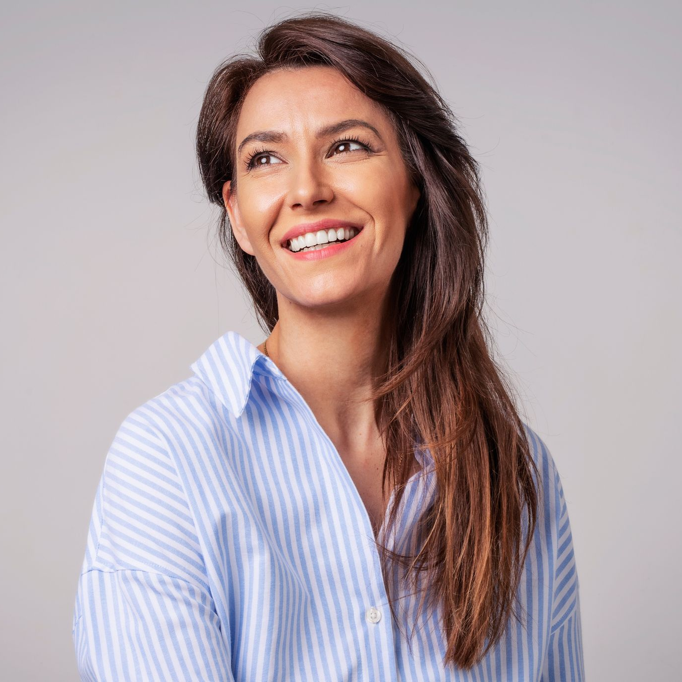 Smiling woman in a light blue striped shirt against a plain gray background