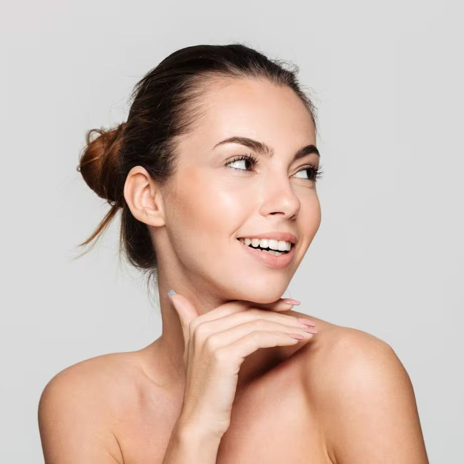Smiling woman with hair in a bun resting her chin on her hand against a light gray background