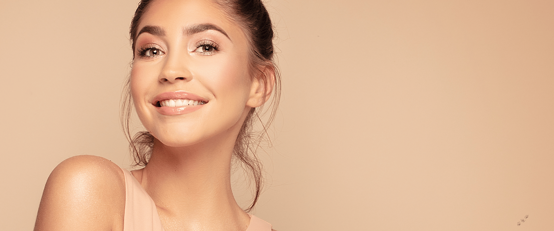 Smiling woman with glowing skin against a soft beige background