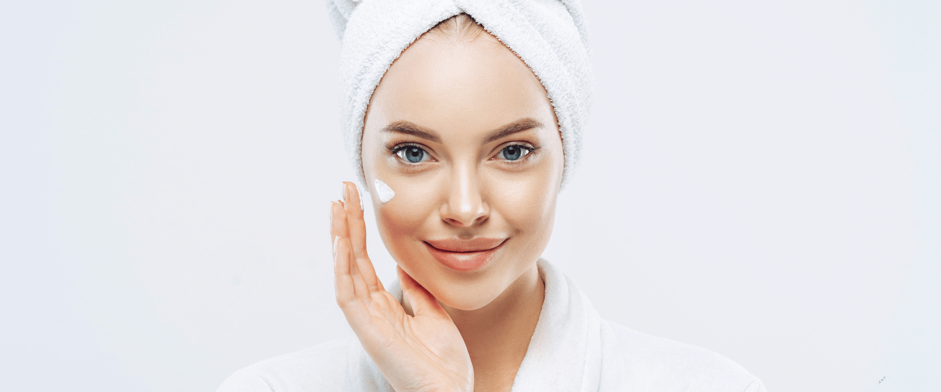 Smiling woman in white towel touching her face against a white background