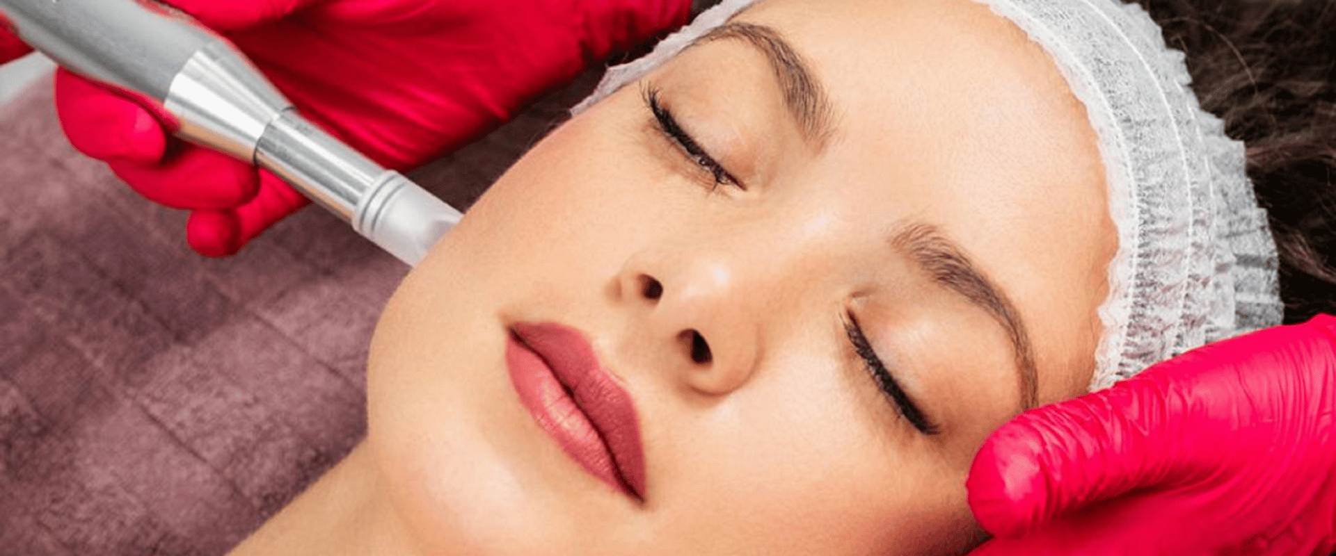 Cosmetic facial treatment with a woman lying down while a gloved technician uses a handheld device on her cheek
