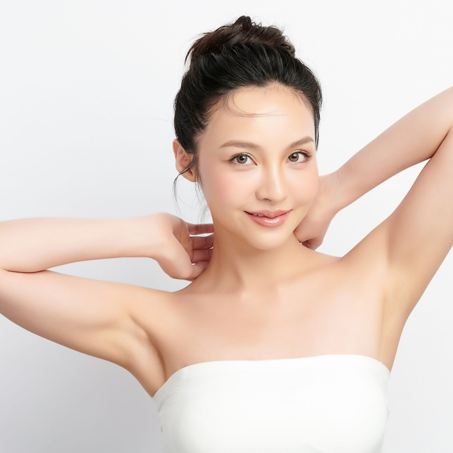 Woman with dark hair in a white strapless top, smiling with arms raised against a light background