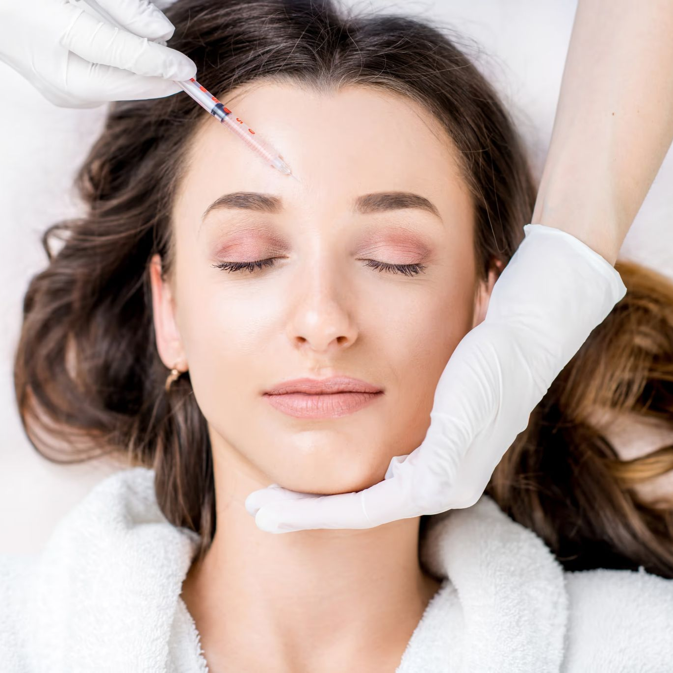 Aesthetic facial treatment with a syringe near a woman’s forehead as she lies on a spa bed