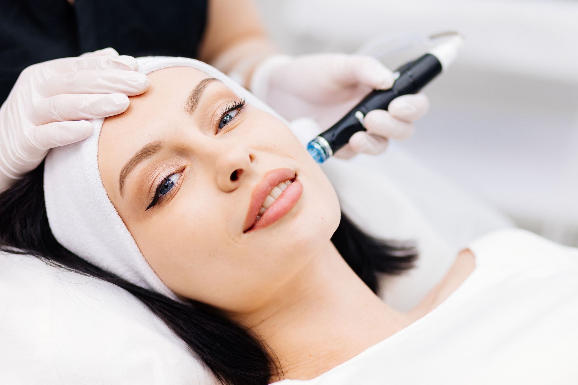 Woman receiving a facial treatment while lying on a spa bed, with a technician using a handheld device.