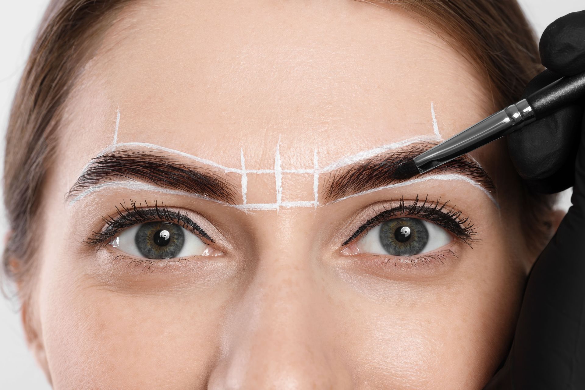 Close-up of eyebrows being shaped with a pencil and makeup guide lines on the forehead