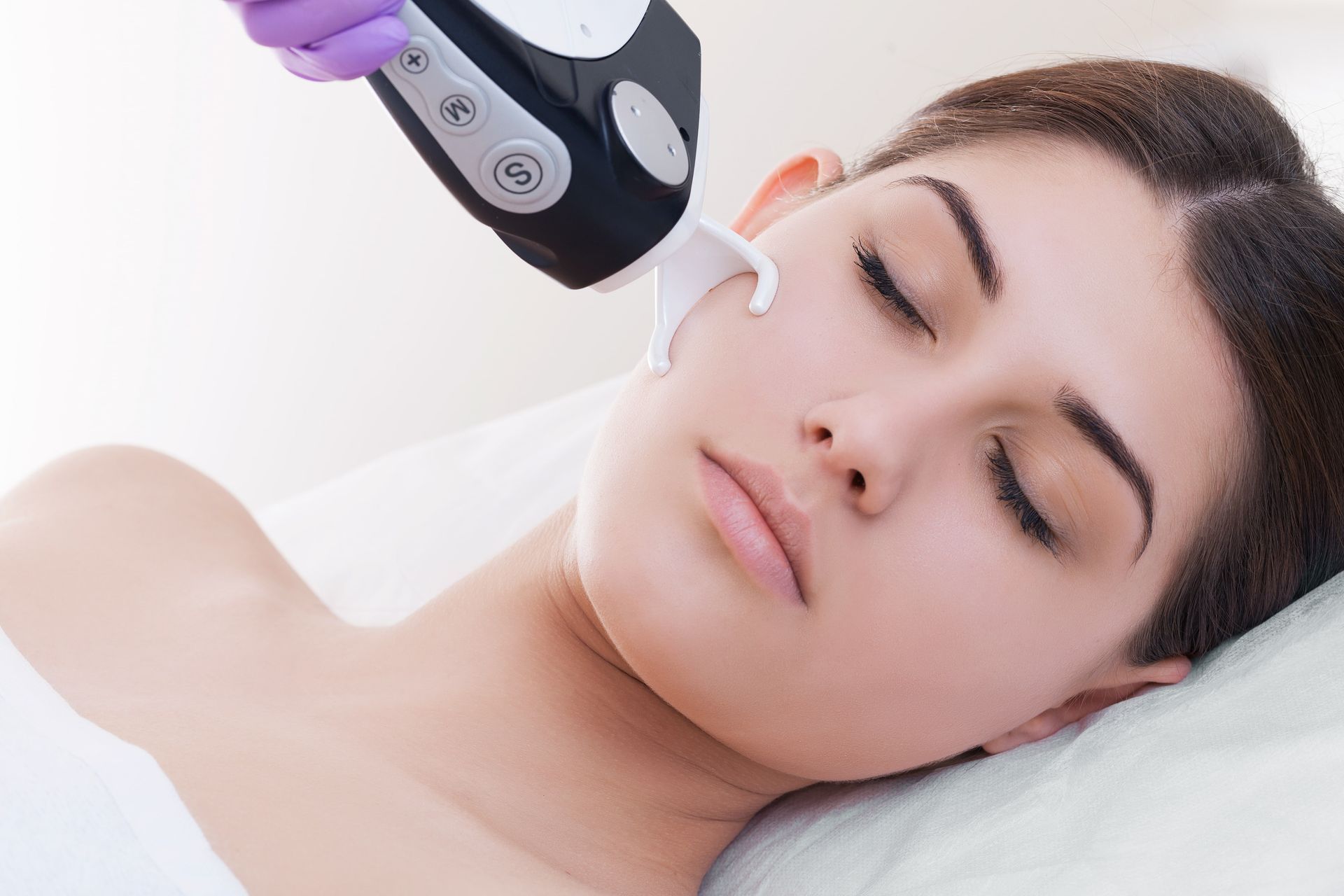 A woman receiving a facial treatment with a handheld device while lying on a spa bed
