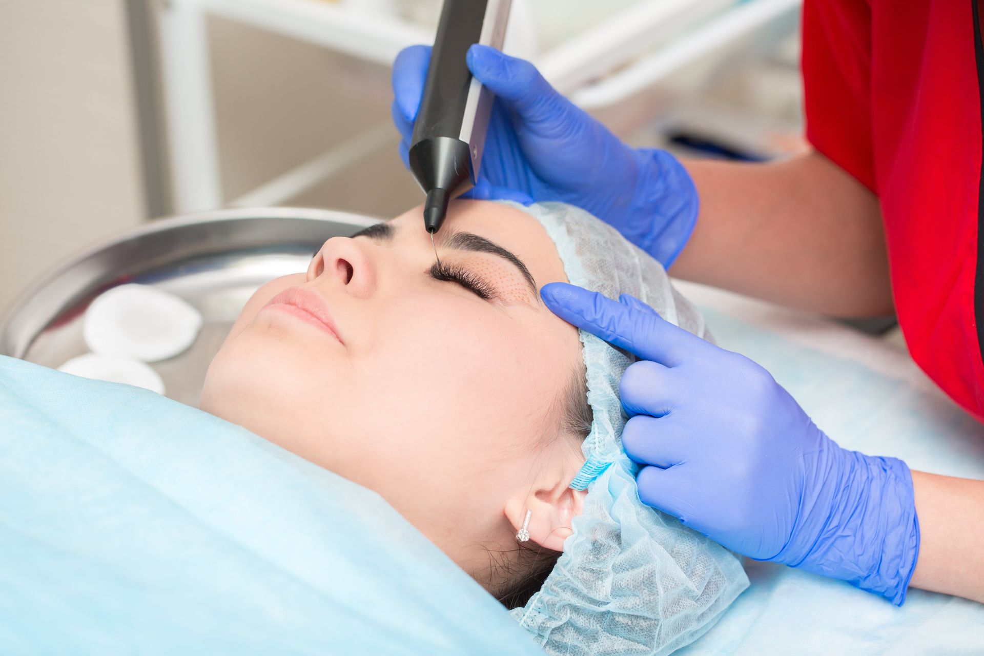 Gloved hands using a handheld device on a woman’s forehead during a cosmetic facial procedure