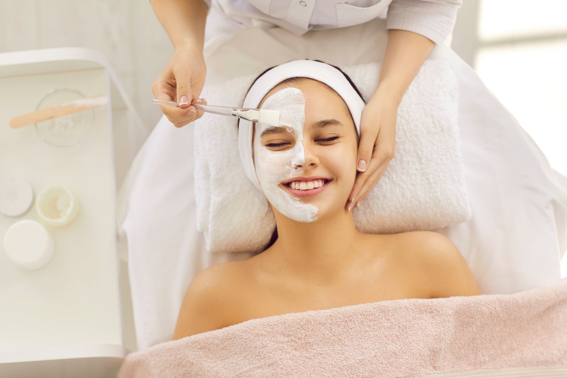 Spa therapist applying a facial mask to a smiling client on a treatment bed