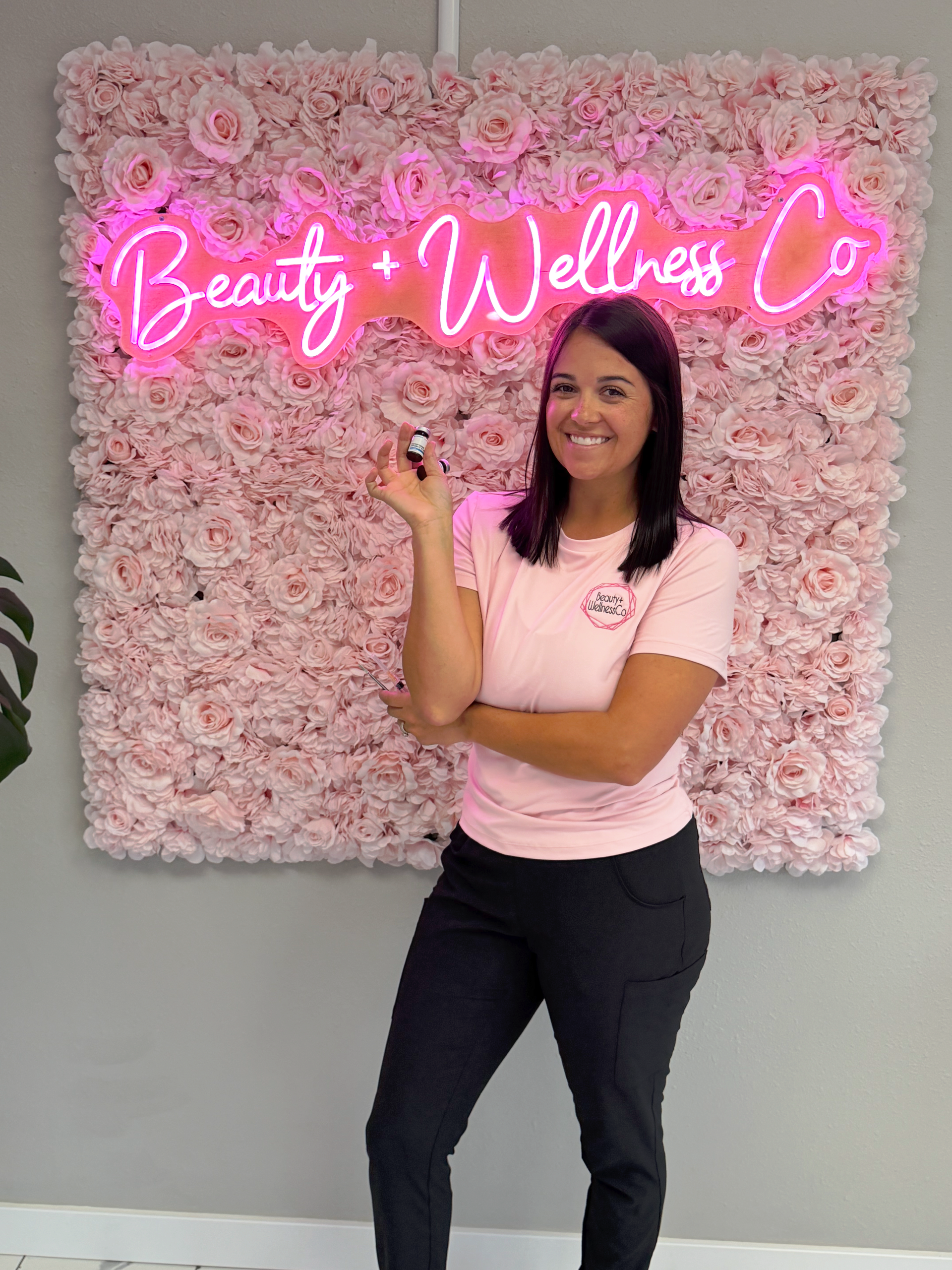 Smiling woman in black outfit standing in a spa room beside shelves of skincare products