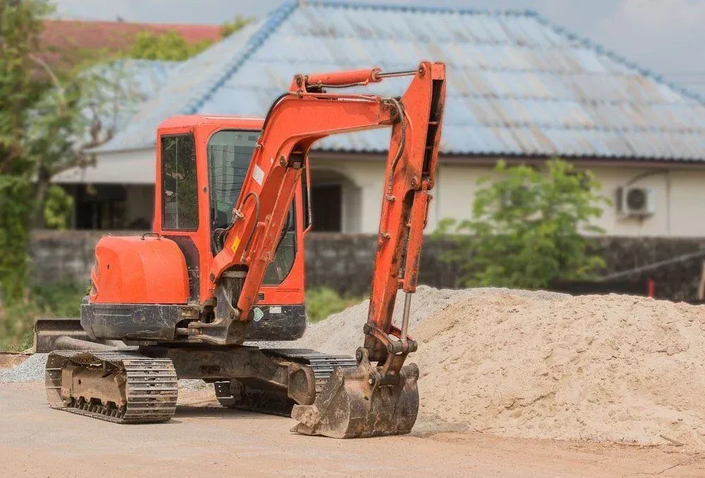 Orange excavator on tracks, parked beside a pile of sand, in front of a house — Far North Plumbing in Mourilyan, QLD