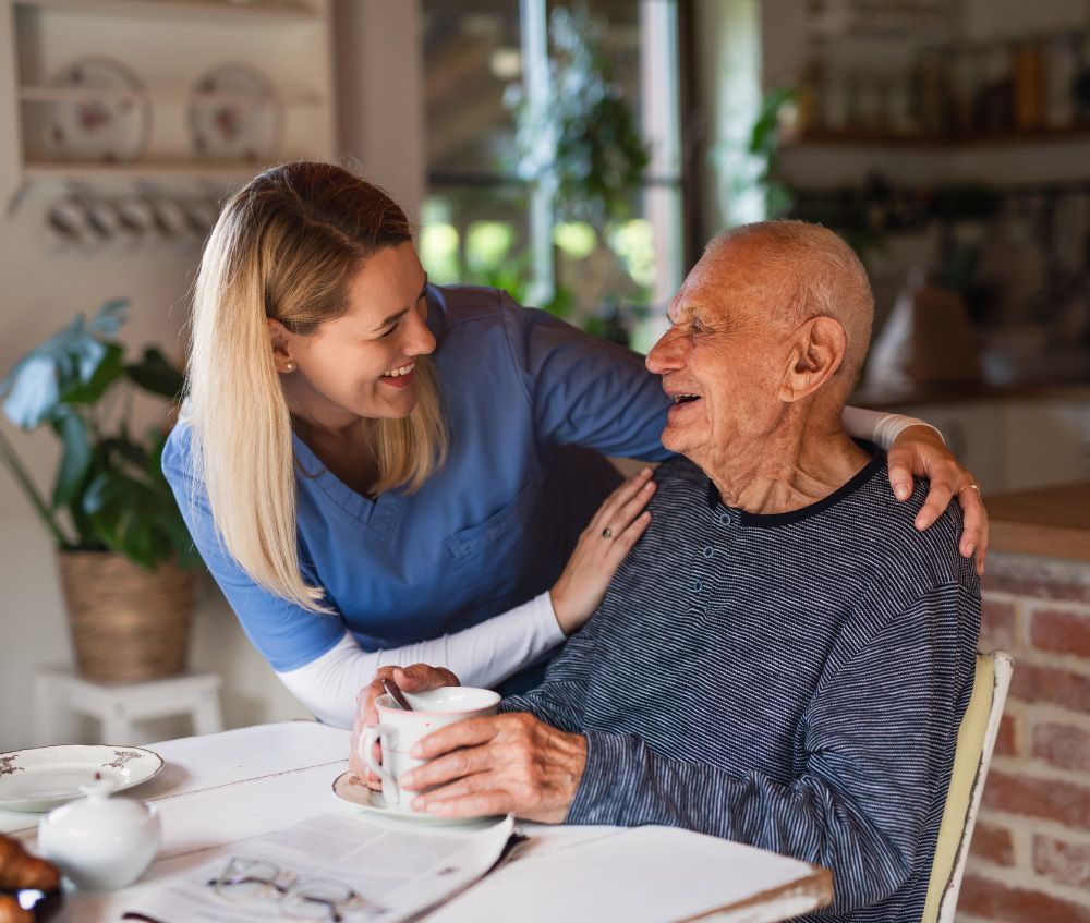 An Elderly Man is Sitting at a Table with a Nurse — Fishers, IN — Alluring Warmth Home Care LLC An Elderly Man is Sitting at a Table with a Nurse — Fishers, IN — Alluring Warmth Home Care LLC