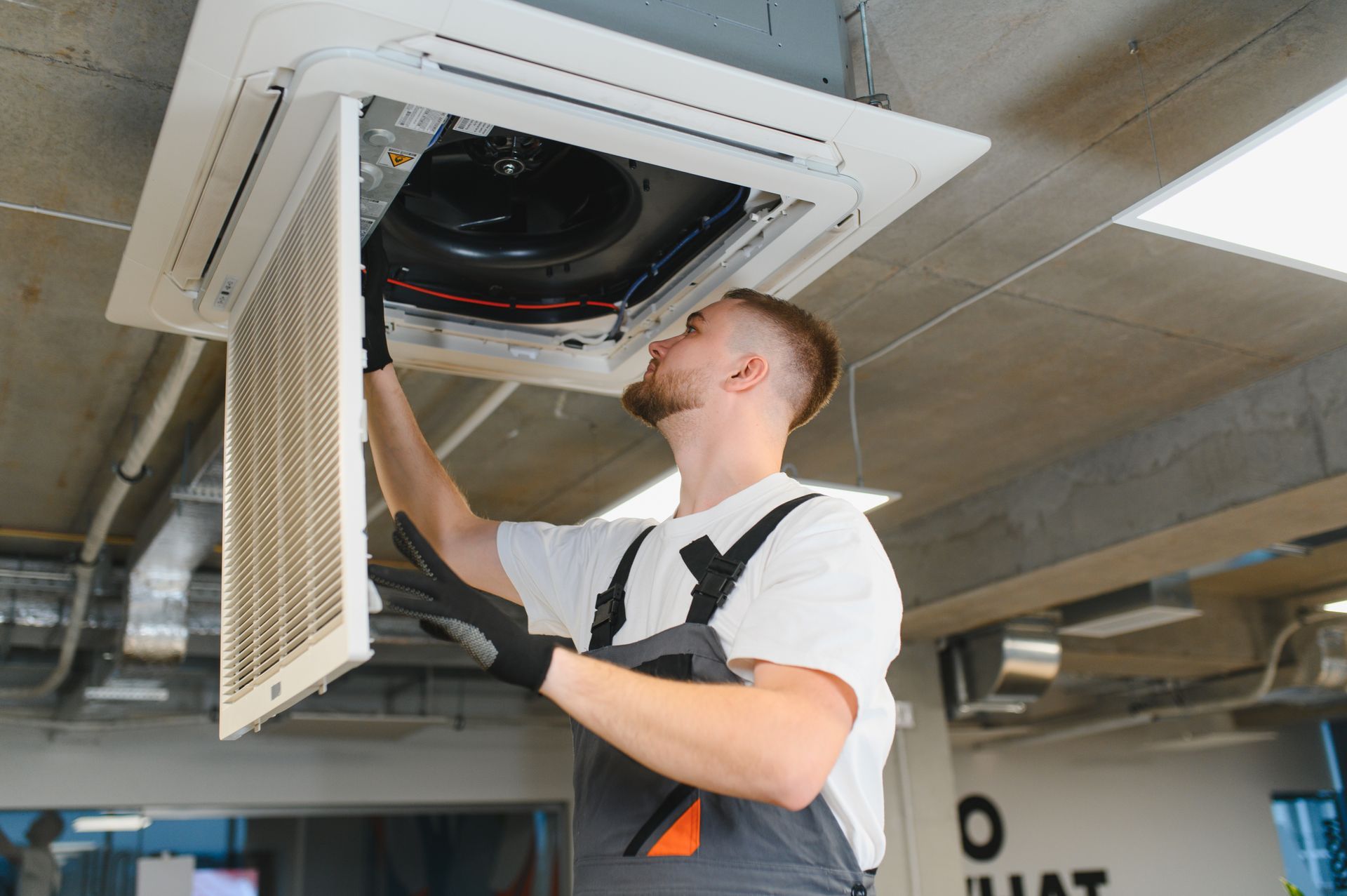 Technician inspecting a ceiling cassette air conditioner with the access panel open