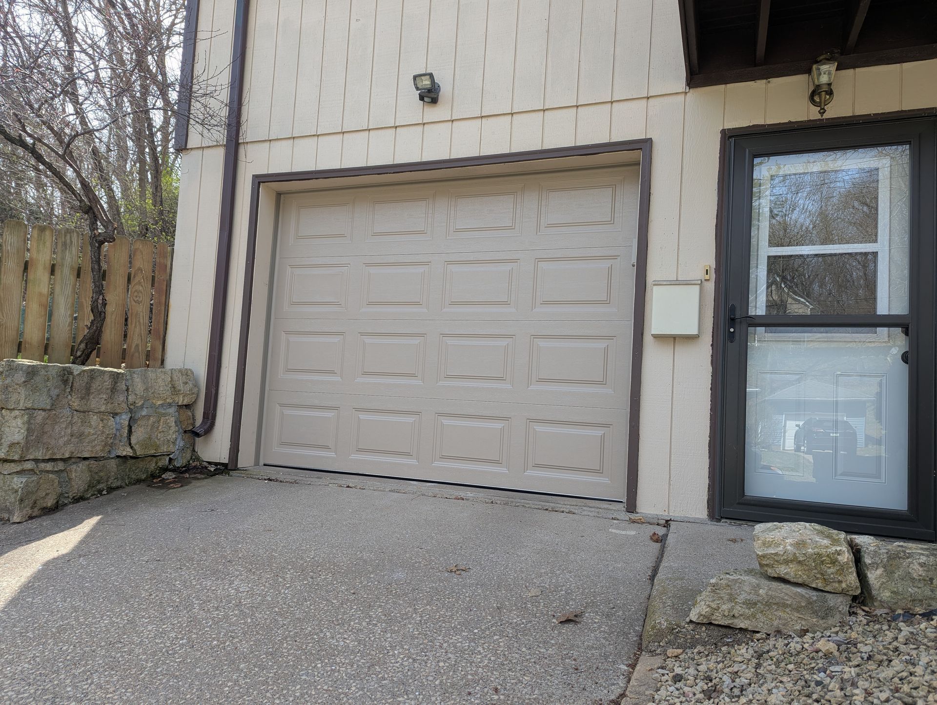 Residential garage with beige door, driveway, and a window beside the entrance