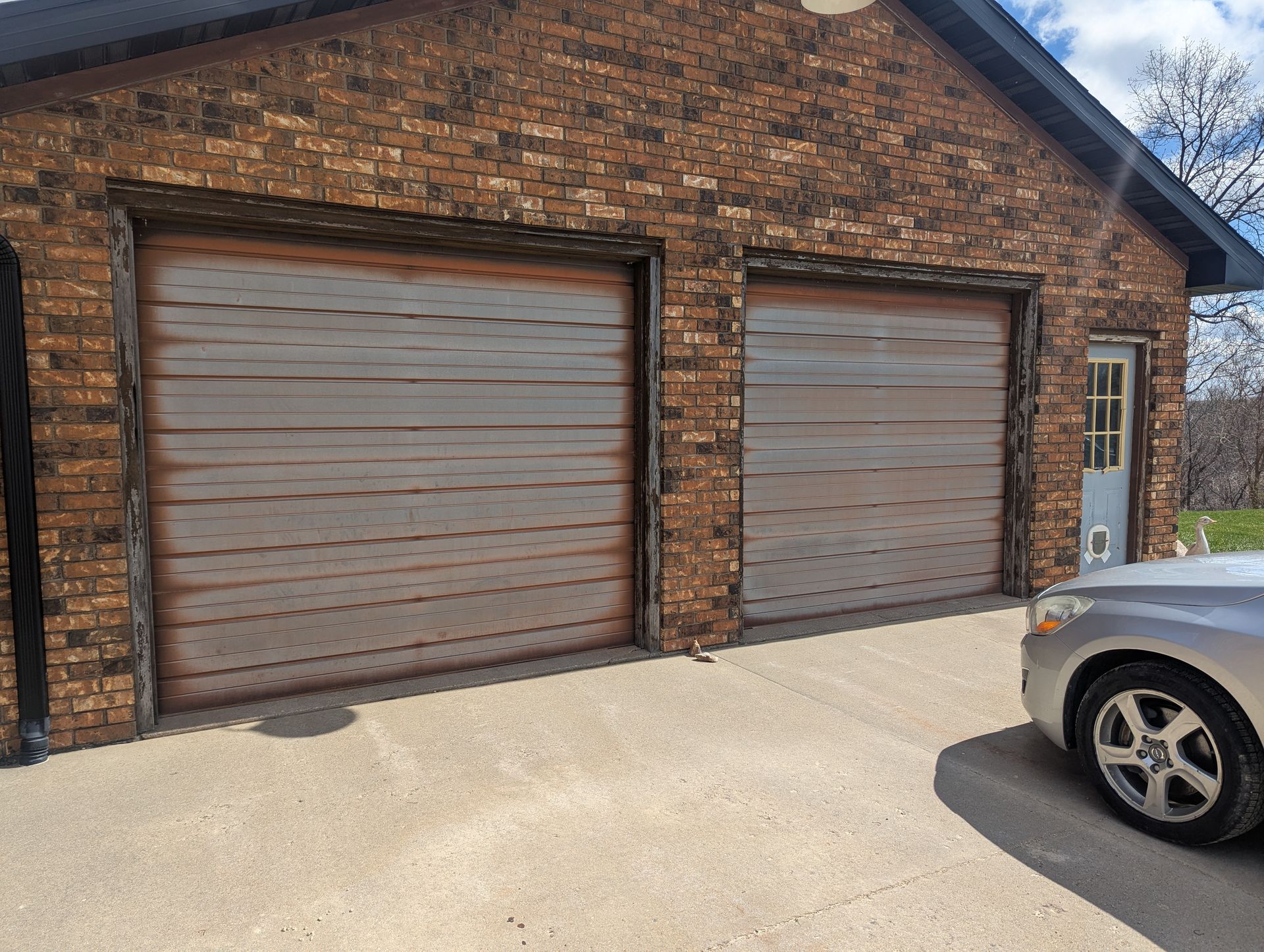 Brick garage with two closed brown doors and part of a silver car in the driveway