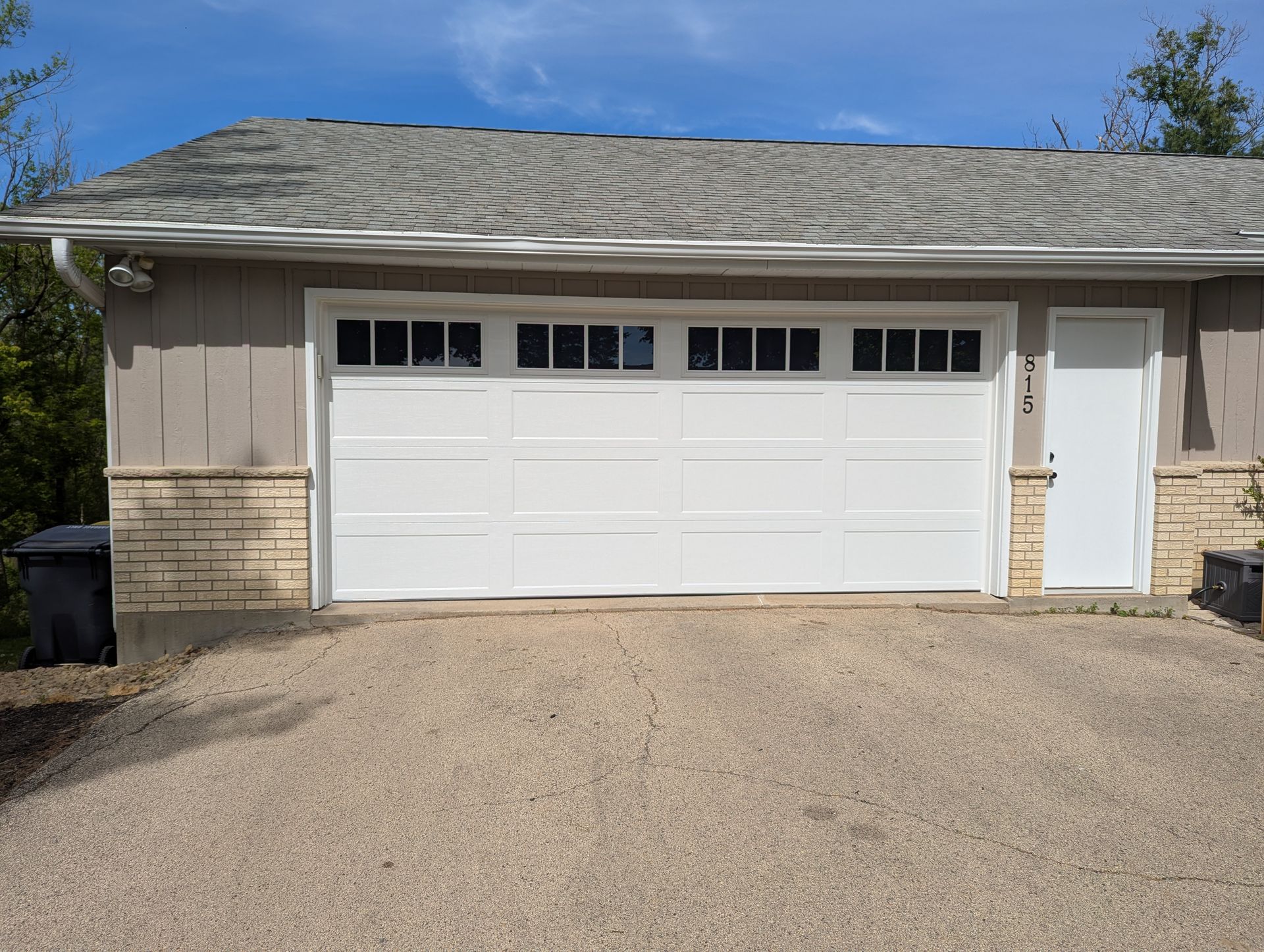 Single-story garage with white door and side entrance, tan exterior, and gravel driveway under a blue sky