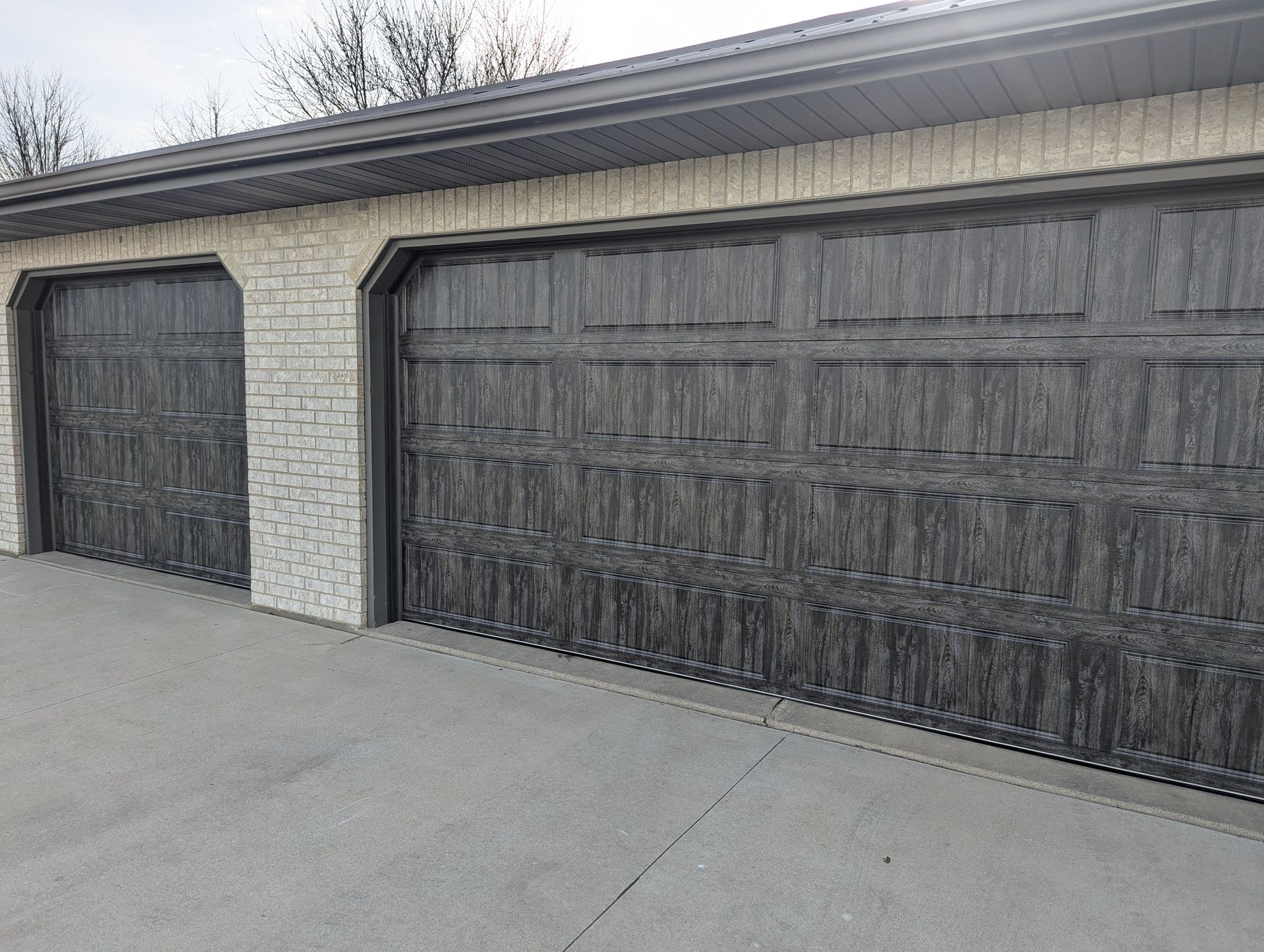 Two black garage doors on a beige house with a concrete driveway